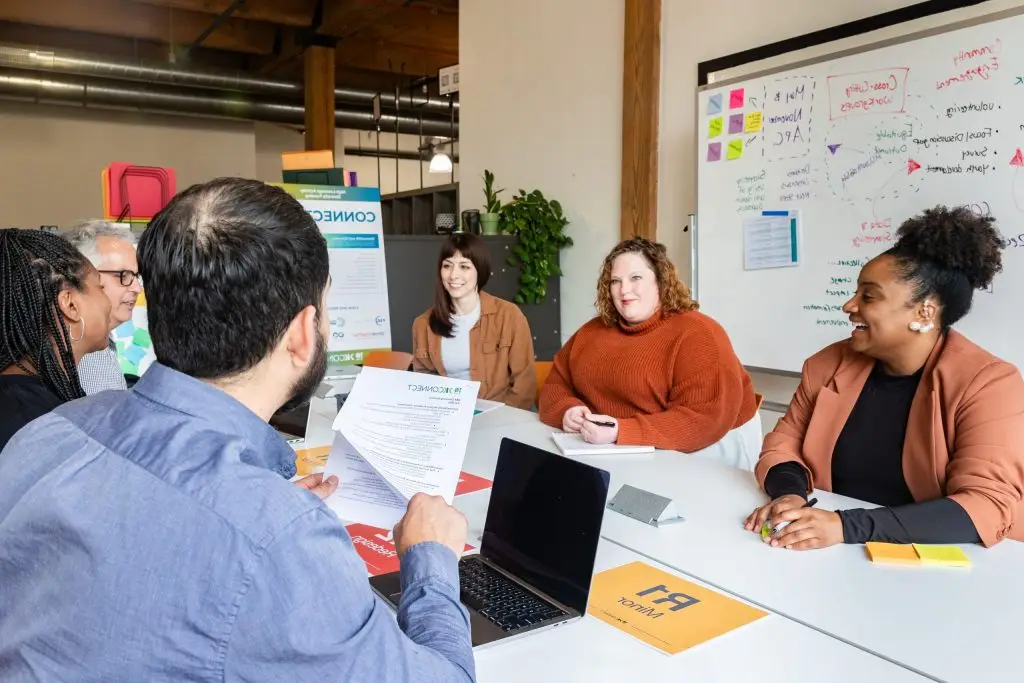 Diverse team of non profit youth organizations collaborating around a conference table with strategic planning materials and whiteboard in background