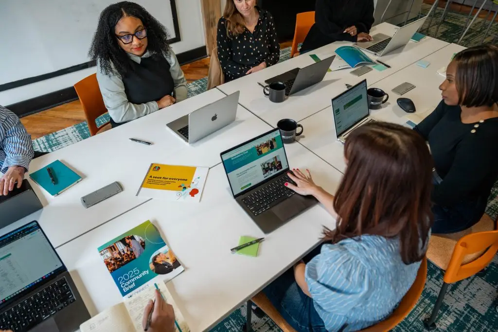 The KConnect team sits at a large table with laptops, print outs, and other branded documents.