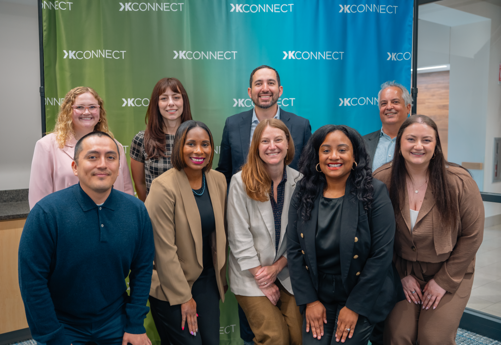 KConnect team members are smiling in front of a KConnect photo banner.